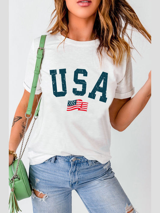 White USA round neck short sleeve t-shirt with flag graphic, paired with ripped jeans and green handbag.