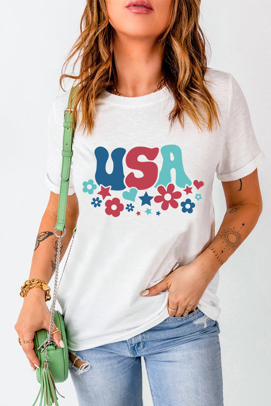 Woman wearing white USA round neck short sleeve T-shirt with colorful floral and star design, paired with light blue jeans and green purse.