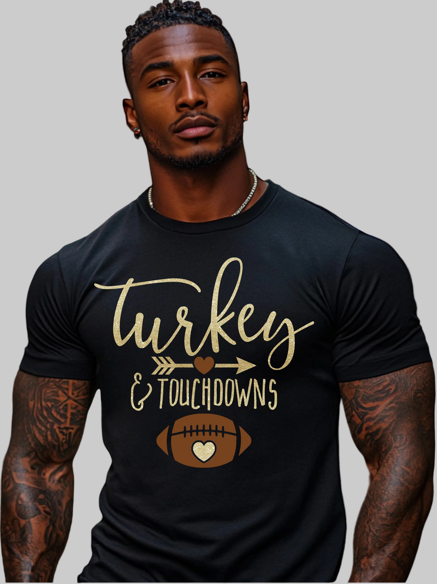 A muscular man with tattoos wearing a black t-shirt with a gold and brown graphic that reads 'Turkey & Touchdowns' with a football design, set against a plain white background - NicholesGifts