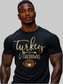 A muscular man with tattoos wearing a black t-shirt with a gold and brown graphic that reads 'Turkey & Touchdowns' with a football design, set against a plain white background - NicholesGifts