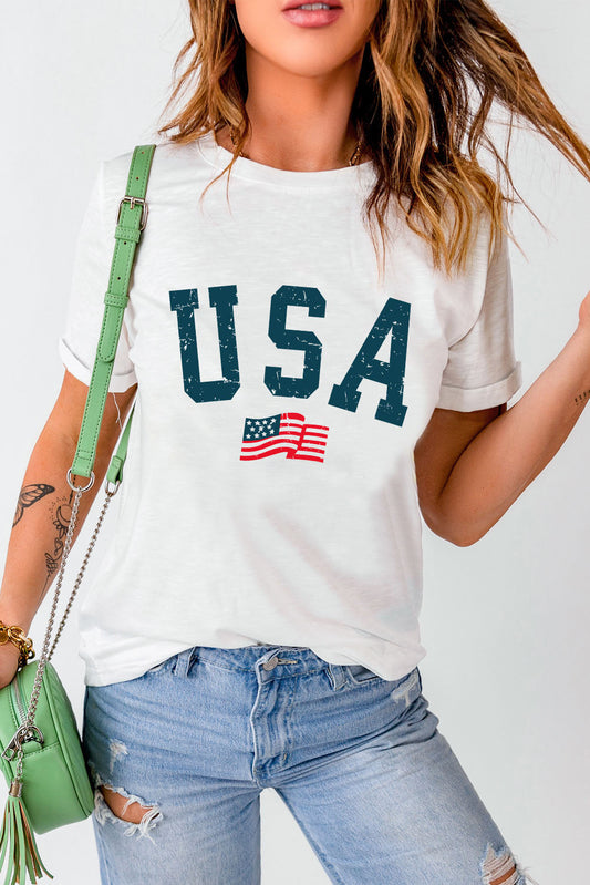 White USA round neck short sleeve t-shirt with flag graphic, paired with ripped jeans and green handbag.